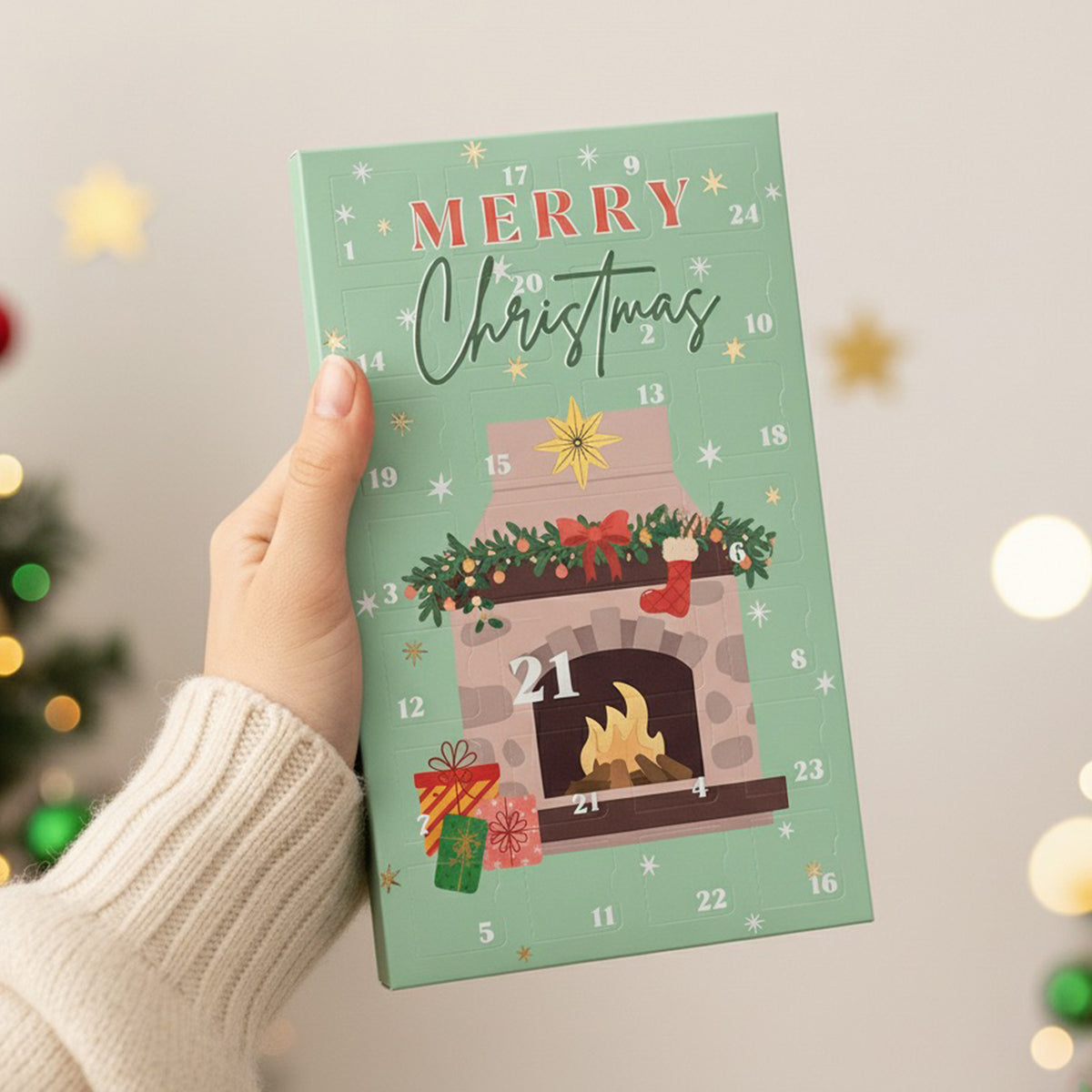 Soy wax melt Advent calendar with festive design held by a hand, Christmas tree and lights in the background