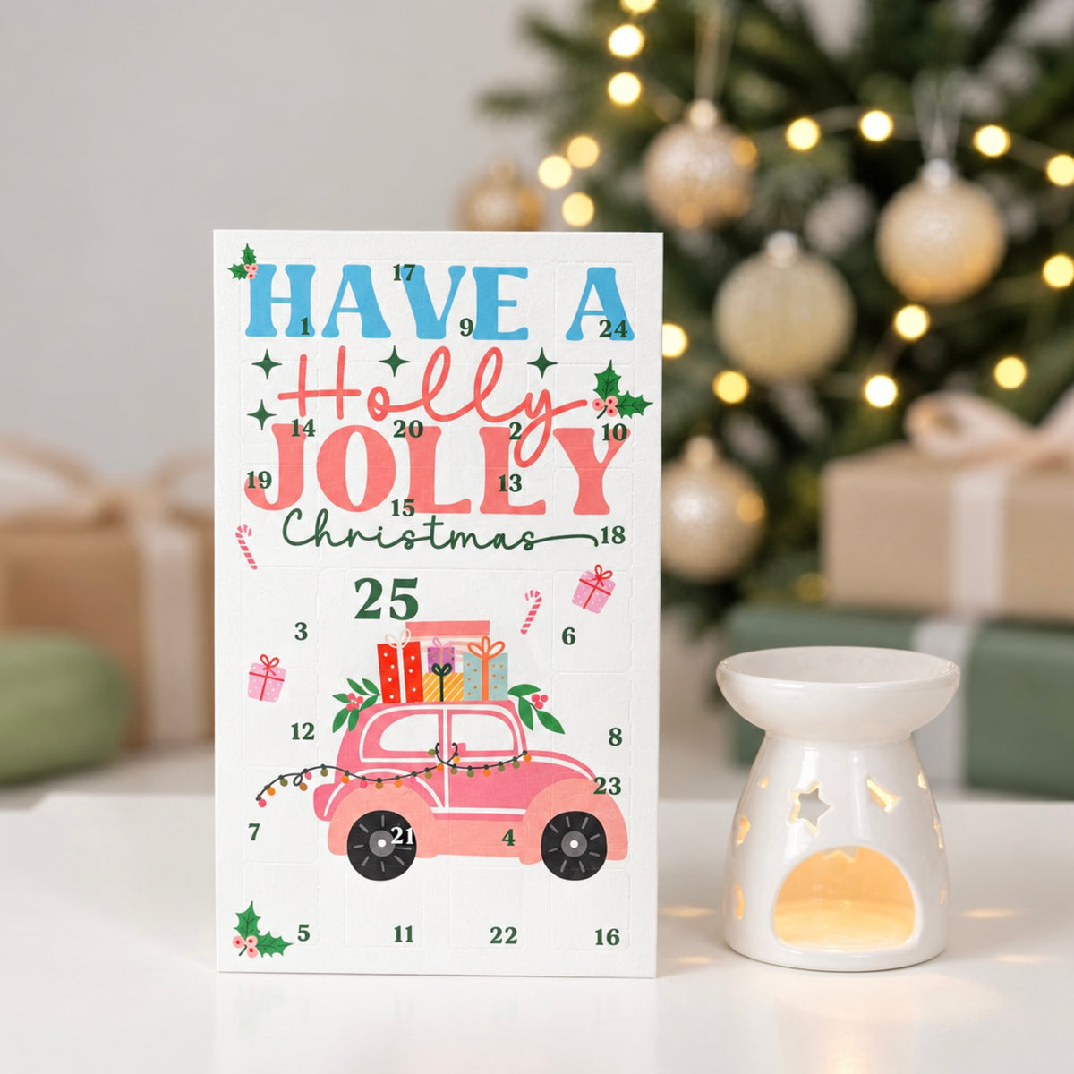 A festive Christmas advent card reading 'HAVE A Holly JOLLY Christmas 25' with a pink car carrying gifts, shown on a white surface beside a white star-cutout candle holder, with a blurred decorated Christmas tree in the background.